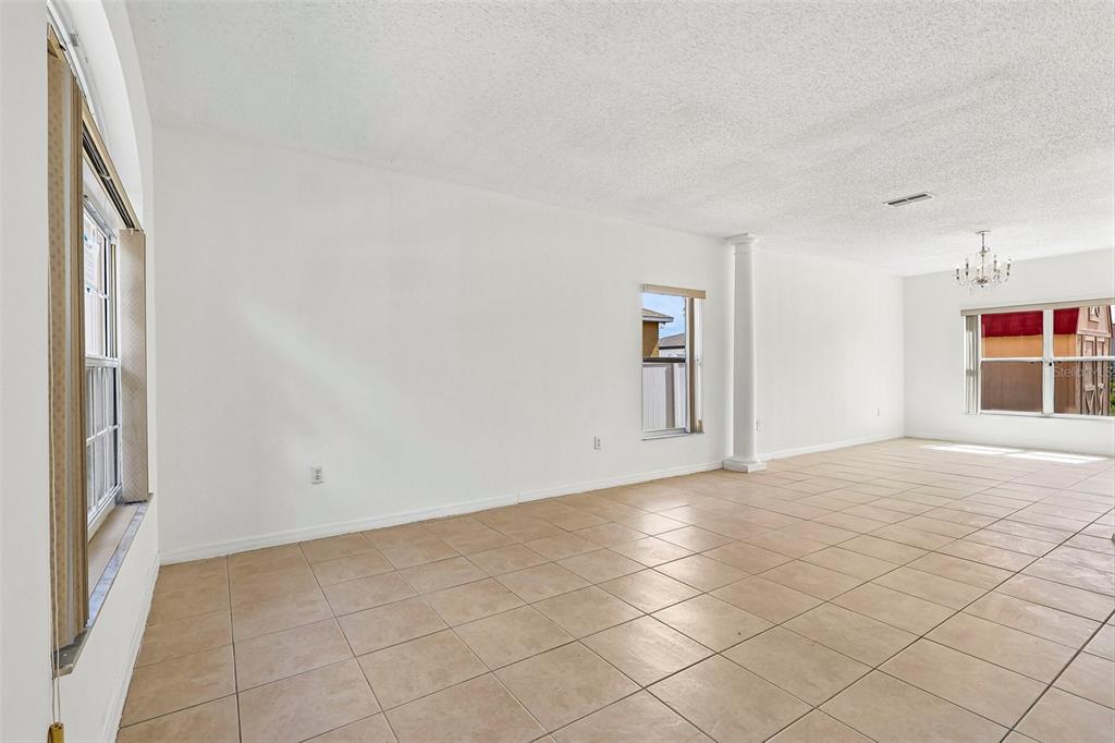 An empty room with beige tile flooring, white walls, a support column, and large windows — 1107 JAMES WAY, POINCIANA, FL