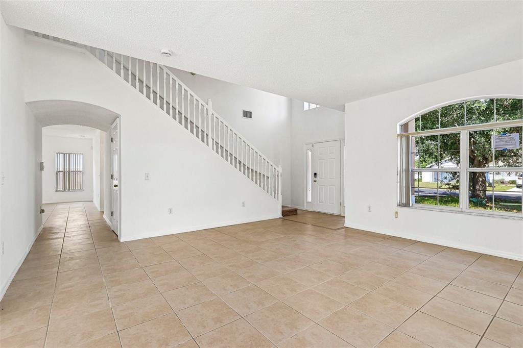 A bright, empty living room features white walls, tile flooring, and a staircase with railings — 1107 JAMES WAY, POINCIANA, FL