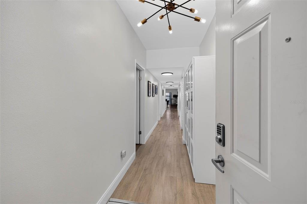 A long hallway with light wood-look flooring, white walls, and a modern sputnik chandelier — 602 LIME AVENUE UNIT 101, CLEARWATER, FL