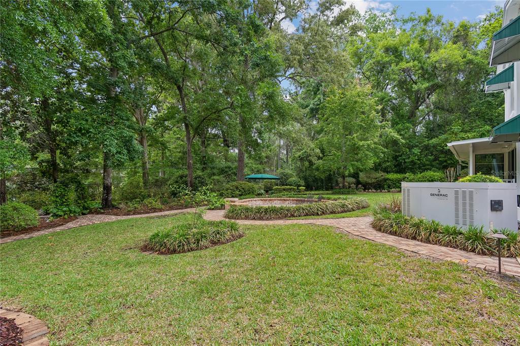 A backyard features a brick paver path, a circular garden bed, and a Generac generator — 2006 NW 23RD STREET, GAINESVILLE, FL