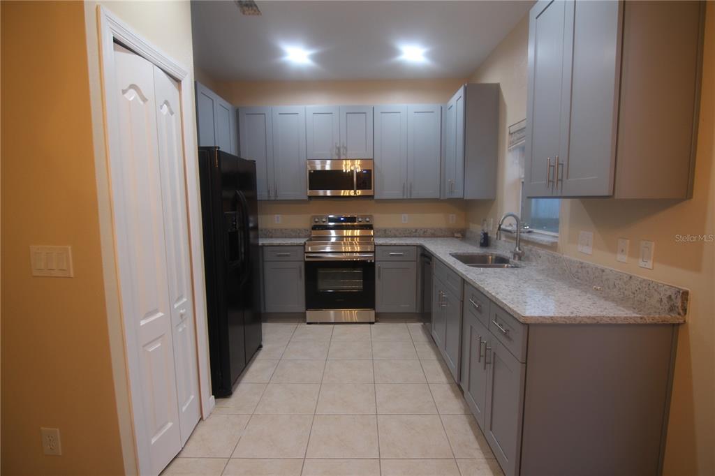 A kitchen features gray cabinets, granite countertops, stainless steel appliances, and a black refrigerator — 733 FORTANINI CIRCLE, OCOEE, FL