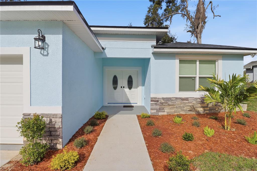 A light blue house exterior features a stone veneer base, double front doors, and landscaping — 822 POPLAR STREET, INVERNESS, FL