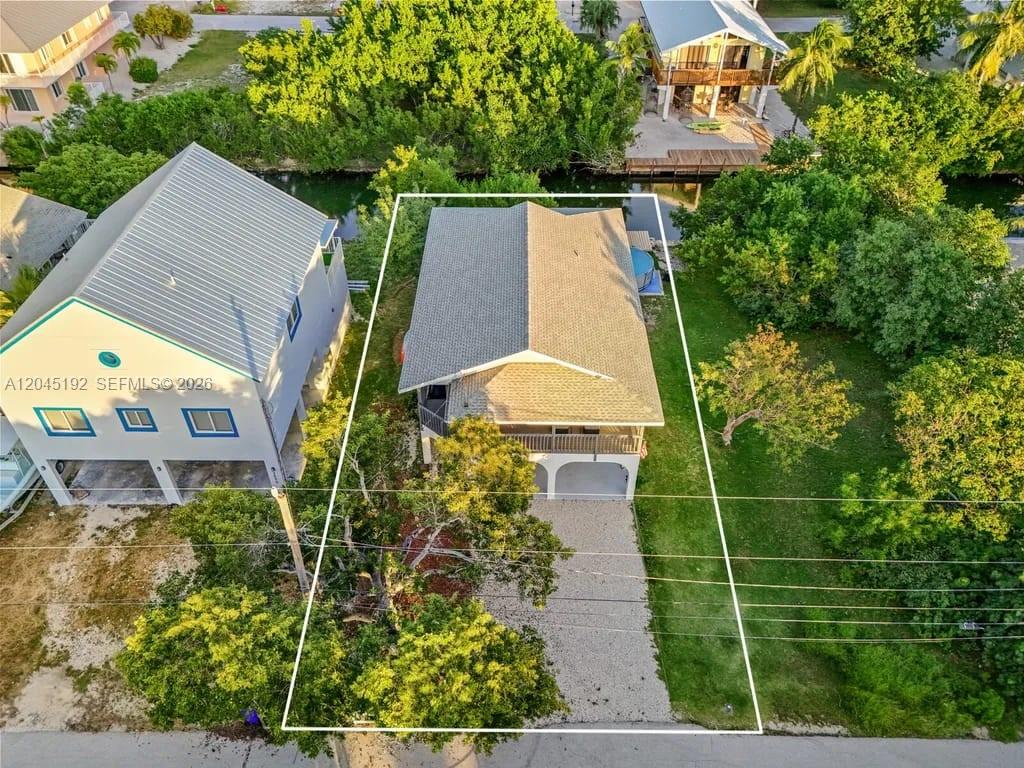 An aerial view shows a house with a gravel driveway and a backyard canal — 3635 Trade Winds St, Big Pine FL 33043, BIG PINE, FL