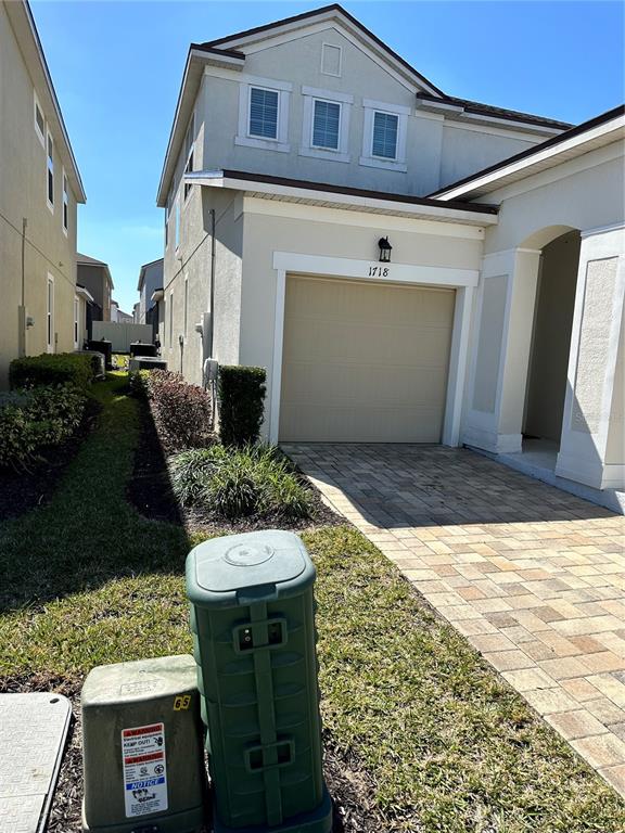 A two-story house exterior features a beige stucco facade, a single-car garage, and a paver driveway — 1718 CARIBBEAN VIEW TERRACE, KISSIMMEE, FL