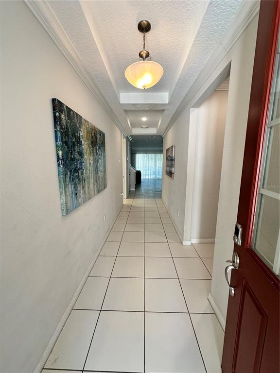 A tiled entryway hallway features a pendant light, a tray ceiling, and abstract wall art — 1718 CARIBBEAN VIEW TERRACE, KISSIMMEE, FL