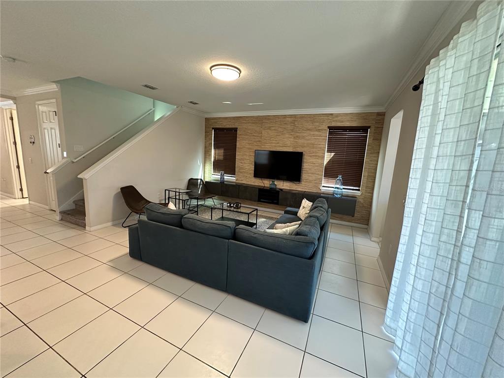 A living room features a blue sectional sofa, a television on a wall-mounted console, and stairs — 1718 CARIBBEAN VIEW TERRACE, KISSIMMEE, FL