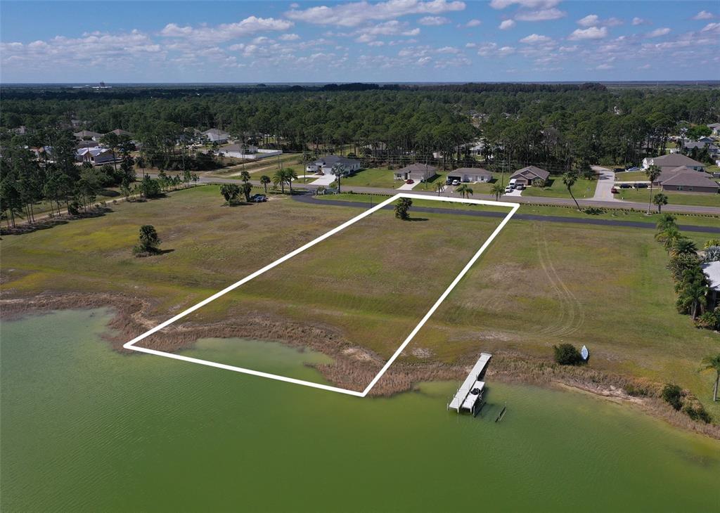An aerial view shows a vacant waterfront lot outlined in white near a residential street — 2565 STILLWATER LAKES DRIVE SW, PALM BAY, FL