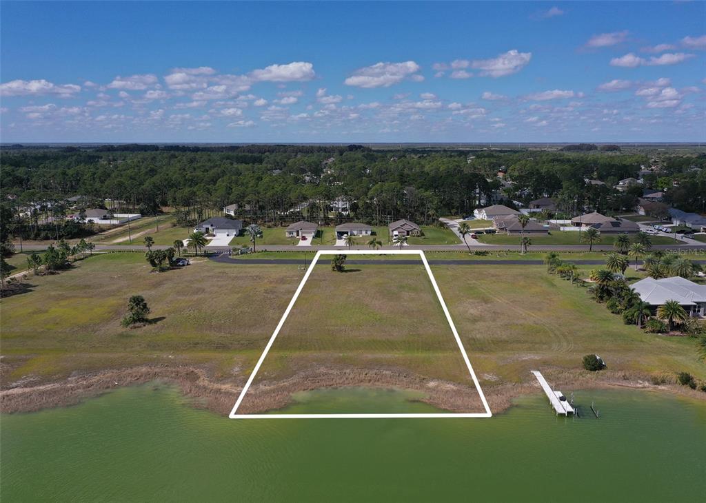 An aerial view shows a vacant waterfront lot outlined in white near a residential street — 2565 STILLWATER LAKES DRIVE SW, PALM BAY, FL