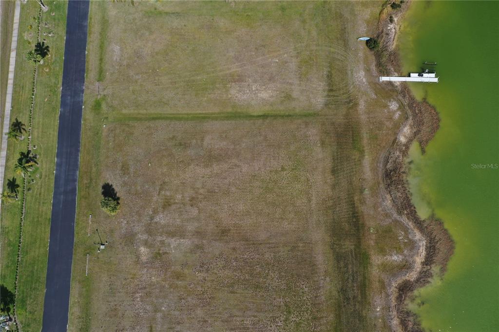 An aerial view shows a vacant grassy lot situated between a paved road and water — 2565 STILLWATER LAKES DRIVE SW, PALM BAY, FL