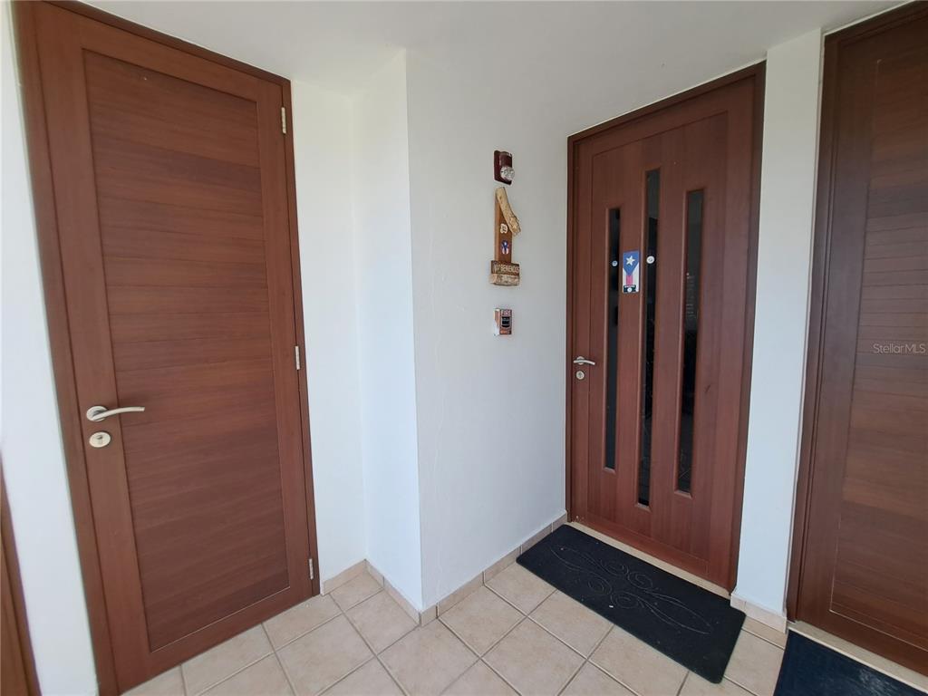 A tiled entryway features three wooden doors and a small wall-mounted decorative sign — A S BUILDING A CORNER S UNIT AC 2, CEIBA, PR