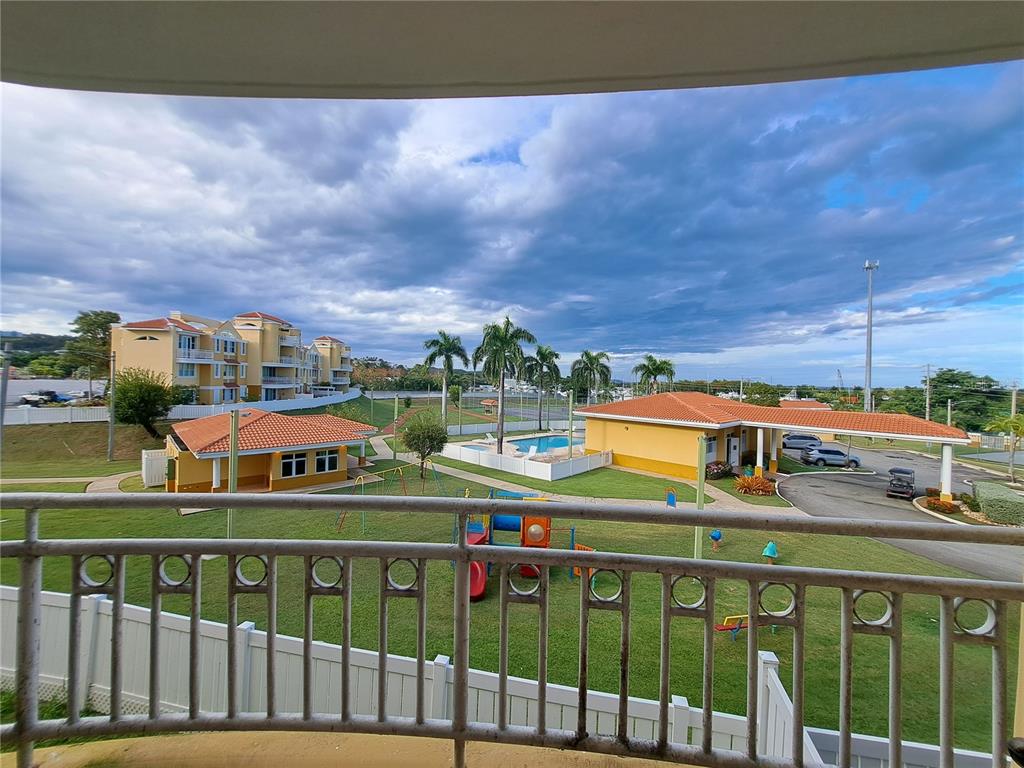 A balcony view overlooks a playground, swimming pool, and apartment buildings under a cloudy sky — A S BUILDING A CORNER S UNIT AC 2, CEIBA, PR