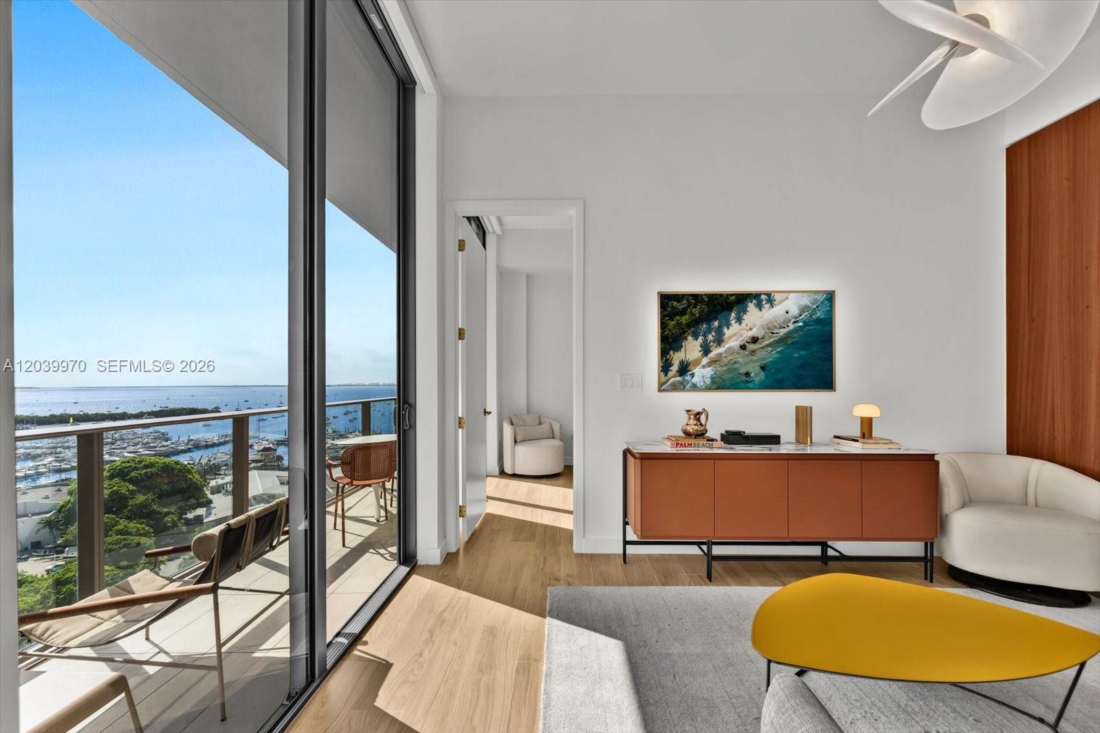 A modern living room features a balcony with water views, a wood console, and seating — 2655 S Bayshore Dr # 1206, Miami FL 33133, MIAMI, FL