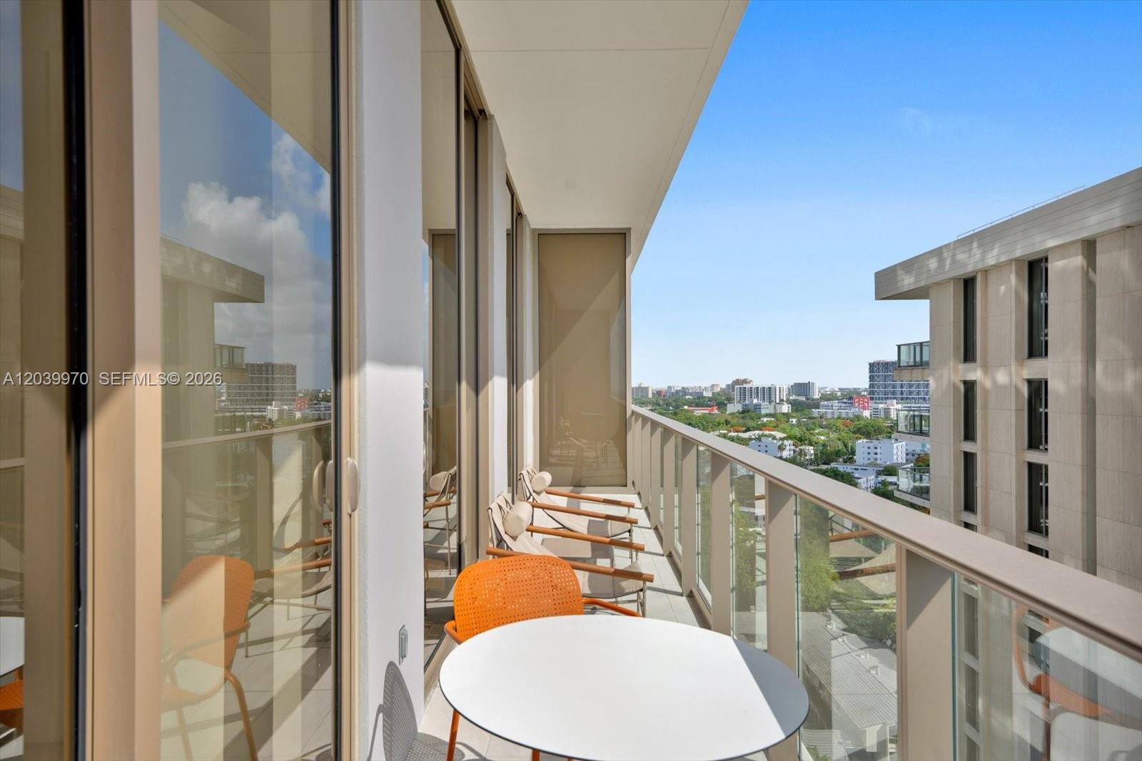 A modern balcony features a small round table, lounge chairs, and a glass railing — 2655 S Bayshore Dr # 1206, Miami FL 33133, MIAMI, FL