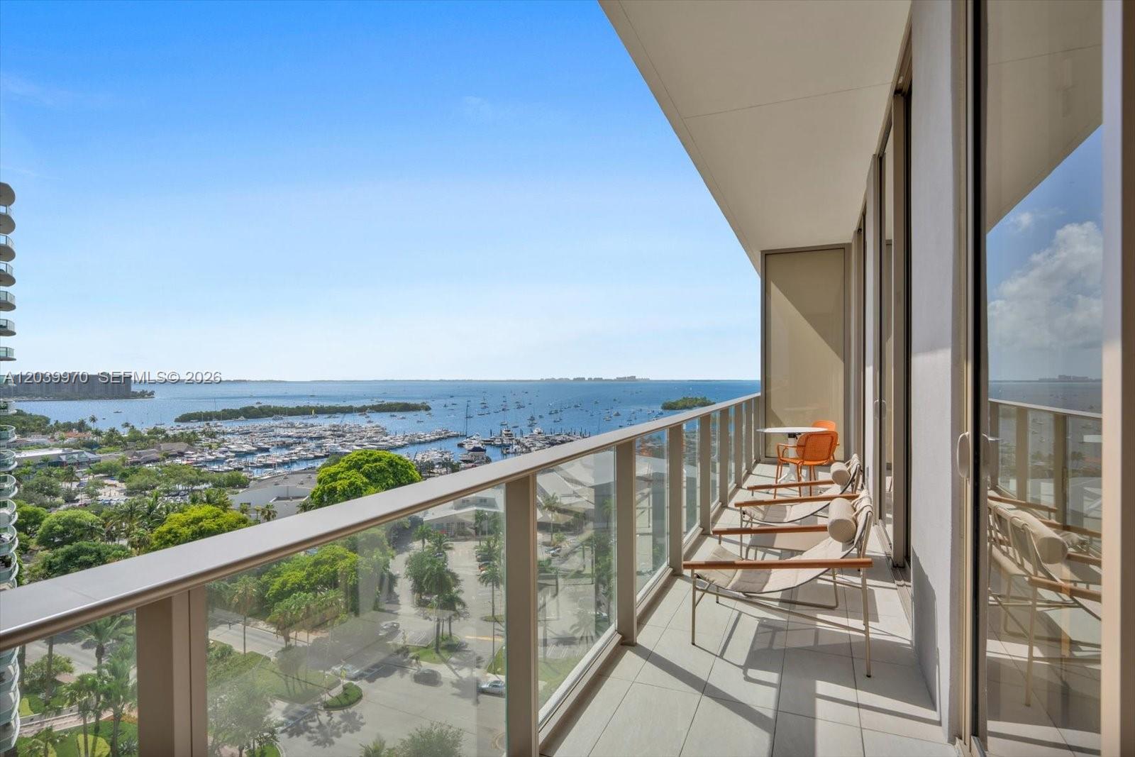 A balcony with glass railings overlooks a marina, trees, and the ocean — 2655 S Bayshore Dr # 1206, Miami FL 33133, MIAMI, FL