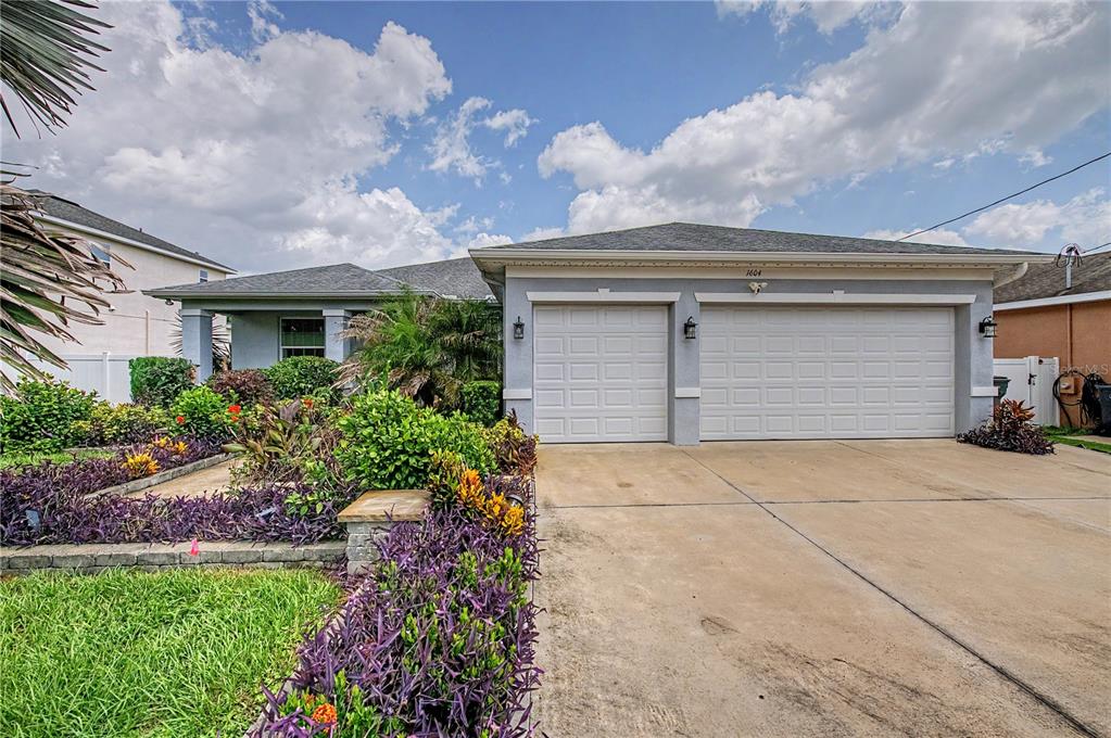 A single-story house with a two-car garage and landscaped front yard under a cloudy sky — 1604 MAIN STREET, VALRICO, FL