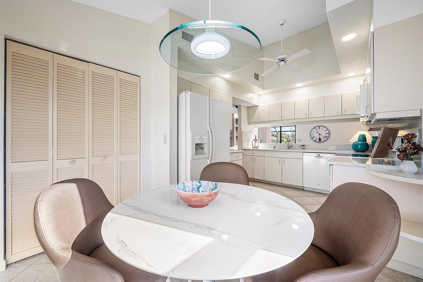 A dining area with a round marble table and chairs sits before a white kitchen — 5722 Willow Creek Lane, Delray Beach FL 33484, DELRAY BEACH, FL