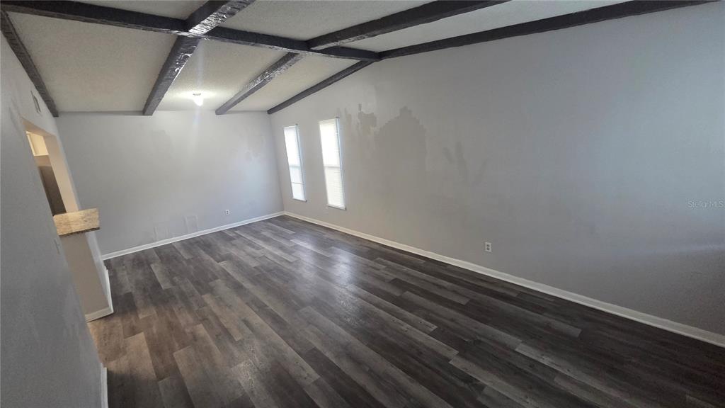 An empty room features gray wood-look flooring, vaulted ceilings with exposed beams, and two windows — 3039 SAINT PAUL DRIVE, WINTER HAVEN, FL