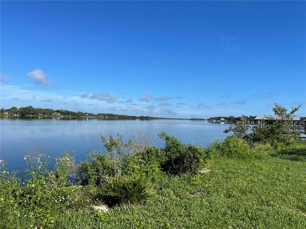 A view of a calm lake from a grassy shoreline under a clear blue sky — 2616 SUNSET DRIVE, NEW SMYRNA BEACH, FL