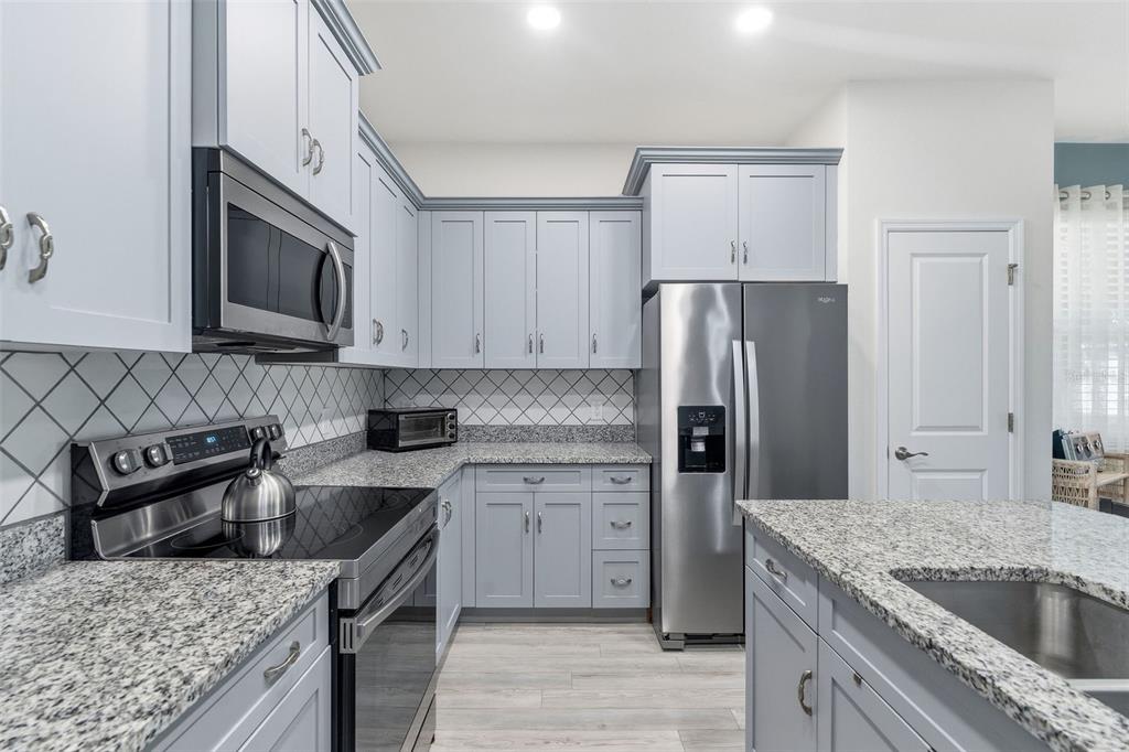 A kitchen features light blue cabinets, granite countertops, stainless steel appliances, and a tiled backsplash — 132 51ST STREET CIRCLE E, PALMETTO, FL