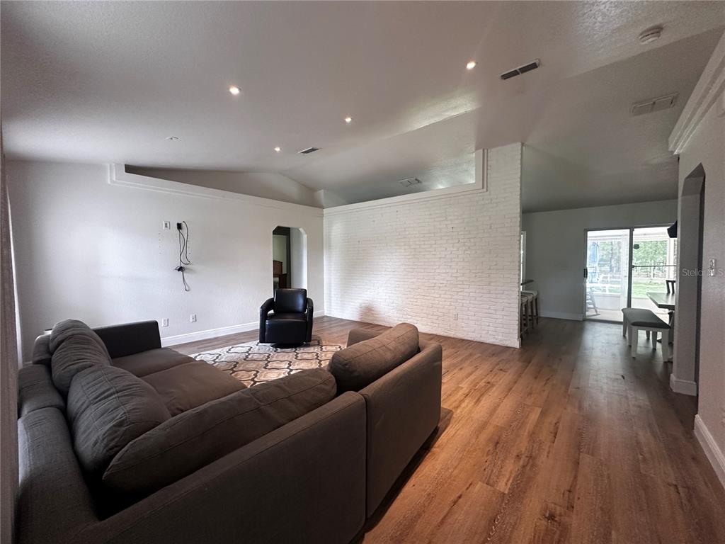 A living room features a grey sectional sofa, a black armchair, and a white brick wall — 11988 SW 38TH STREET, OCALA, FL