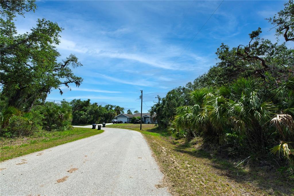 A paved road leads toward a house surrounded by trees and dense vegetation — BACKERT ROAD Lot 15, NORTH PORT, FL