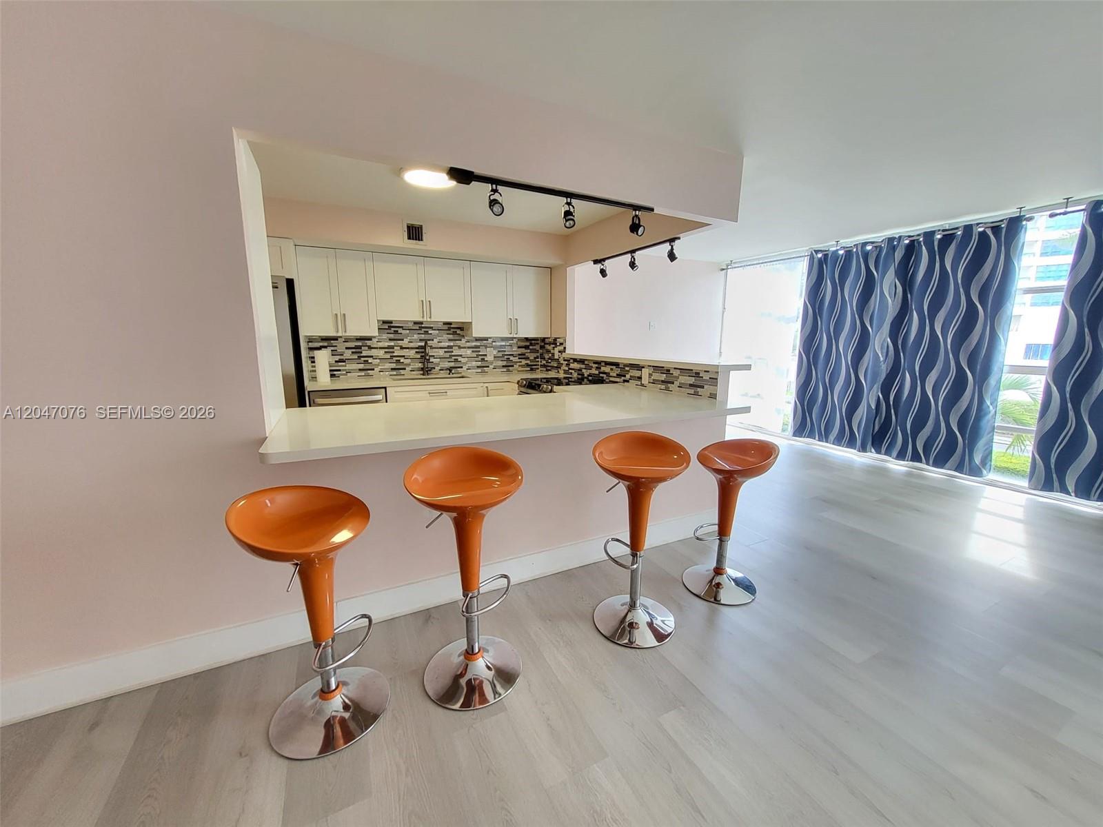 A kitchen with white cabinets and a breakfast bar featuring four orange stools — 501 Three Islands Blvd # 310, Hallandale Beach FL 33009, HALLANDALE BEACH, FL