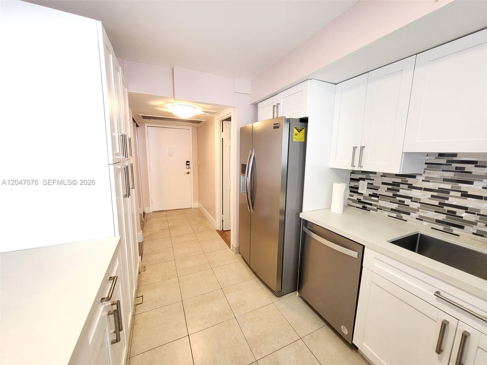 A kitchen features white cabinetry, stainless steel appliances, a tiled backsplash, and light floor tiles — 501 Three Islands Blvd # 310, Hallandale Beach FL 33009, HALLANDALE BEACH, FL