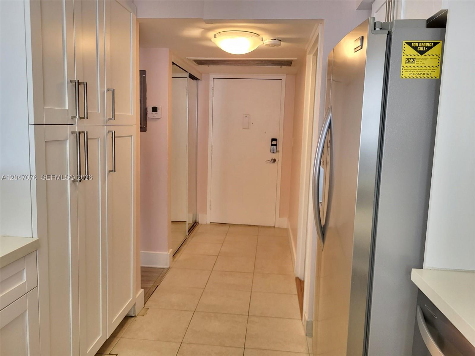 A hallway with white cabinets, a stainless steel refrigerator, and a door at the end — 501 Three Islands Blvd # 310, Hallandale Beach FL 33009, HALLANDALE BEACH, FL