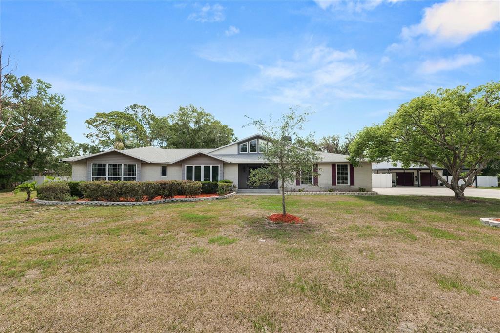 A single-story house with a light-colored exterior, a large lawn, and a detached garage — 6230 FORESTWOOD DRIVE W, LAKELAND, FL