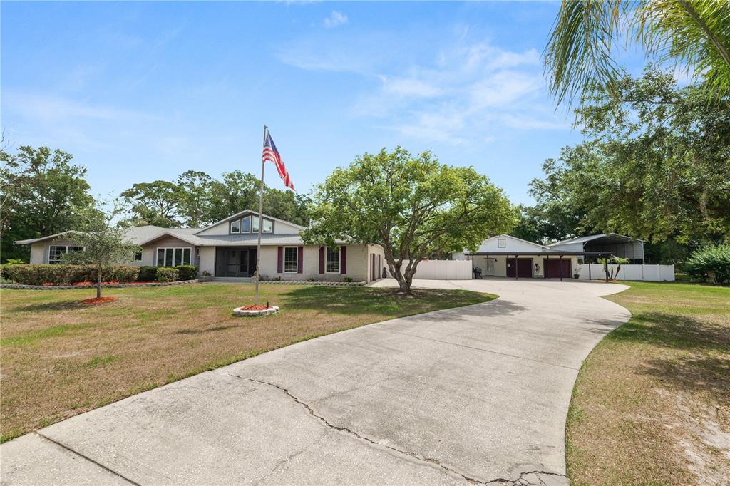 A single-story house with a large driveway, a flag pole, and a detached garage structure — 6230 FORESTWOOD DRIVE W, LAKELAND, FL