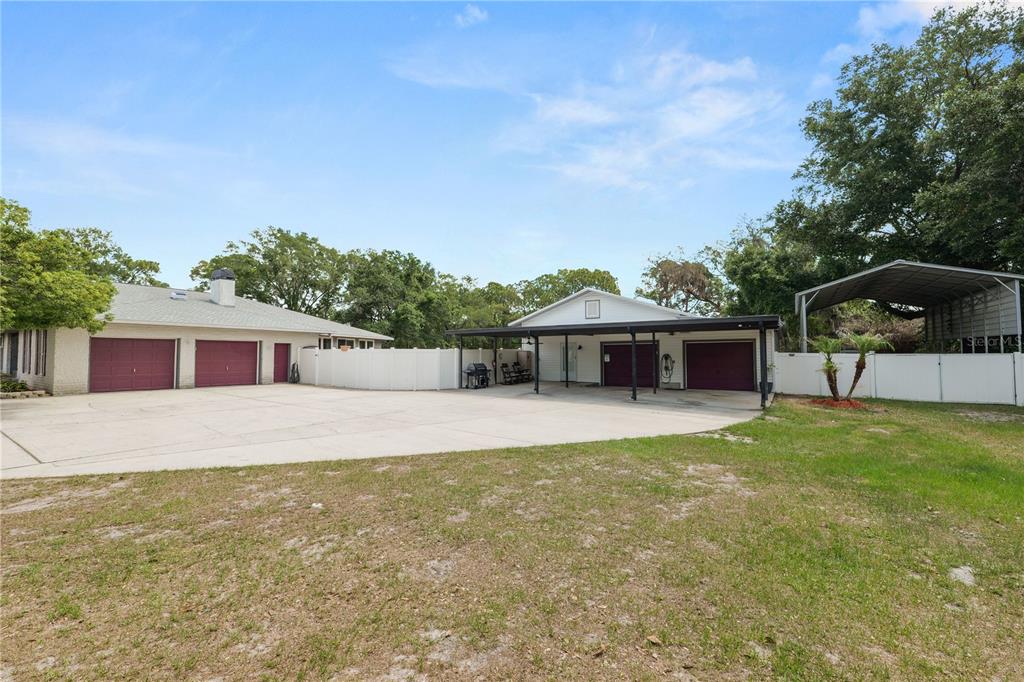 A large concrete driveway sits between two detached garage buildings and a metal carport — 6230 FORESTWOOD DRIVE W, LAKELAND, FL