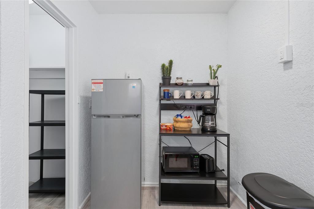 A small kitchen area features a silver refrigerator, a metal shelving unit, and a microwave — 602 POINSETTIA AVENUE, CLEARWATER BEACH, FL