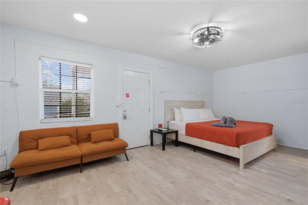 A bedroom features a bed with an orange cover, a sofa, and light-colored flooring — 602 POINSETTIA AVENUE, CLEARWATER BEACH, FL
