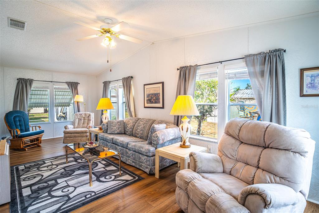 A living room with a patterned sofa, recliner, area rug, and windows with gray curtains — 56 BEAVERKILL DRIVE, LAKE WALES, FL