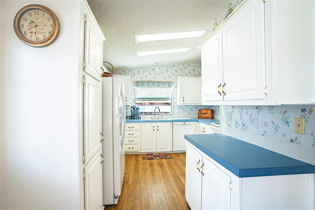 A kitchen with white cabinets, blue countertops, floral wallpaper, and wood-look flooring — 56 BEAVERKILL DRIVE, LAKE WALES, FL