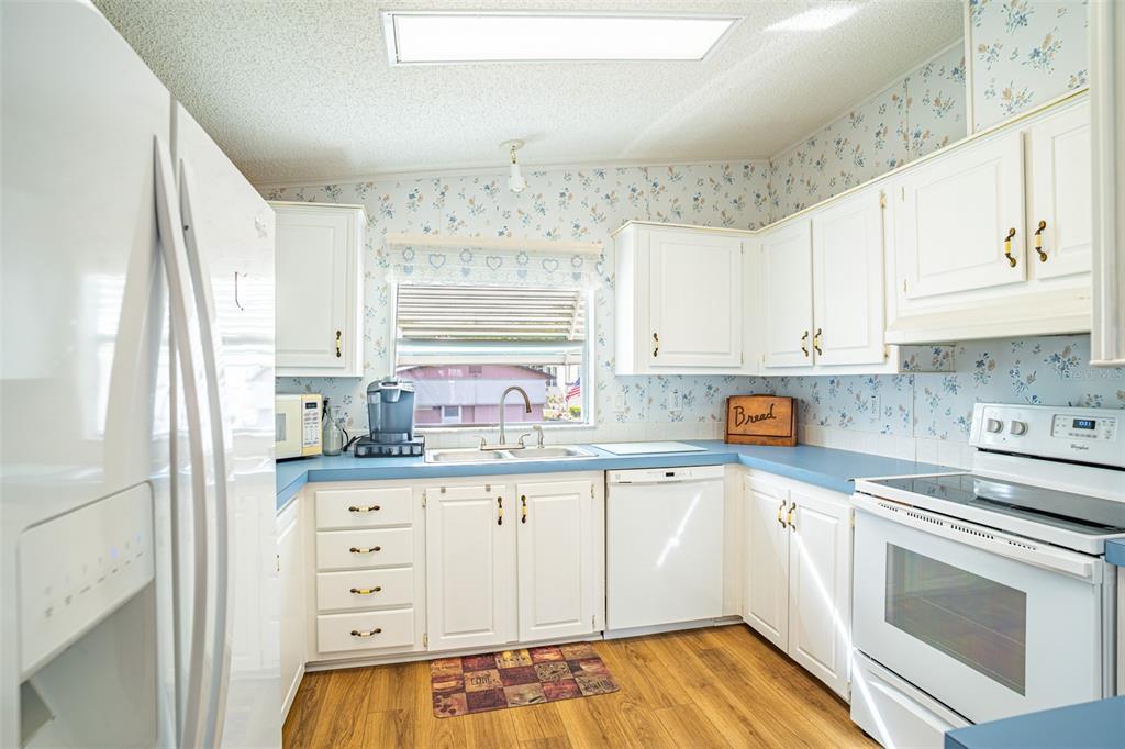 A kitchen with white cabinets, blue countertops, floral wallpaper, and wood-look flooring — 56 BEAVERKILL DRIVE, LAKE WALES, FL