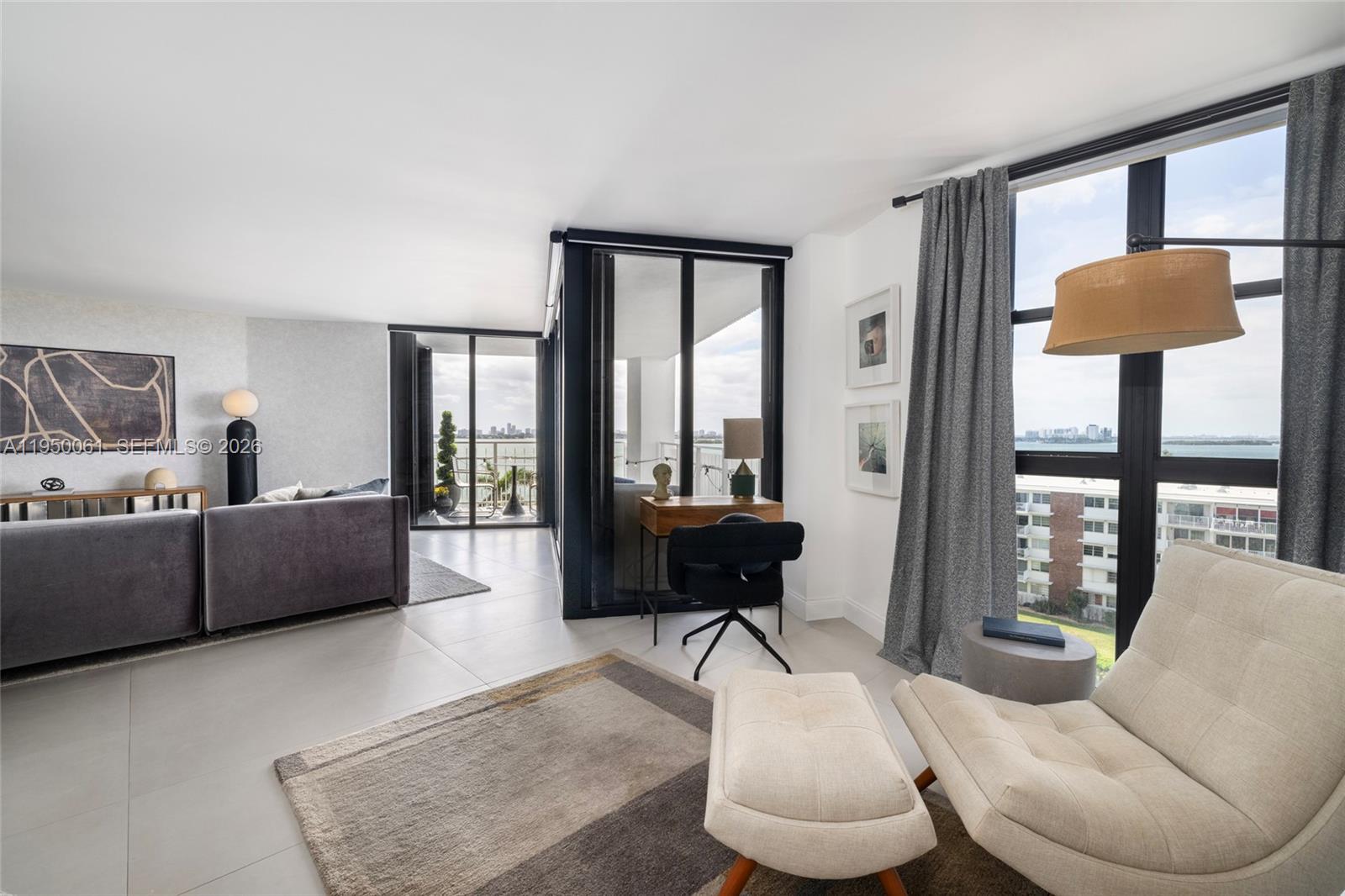 A modern living room features a grey sofa, a desk area, and floor-to-ceiling windows — 4000 Towerside Ter # 804, Miami FL 33138, MIAMI, FL