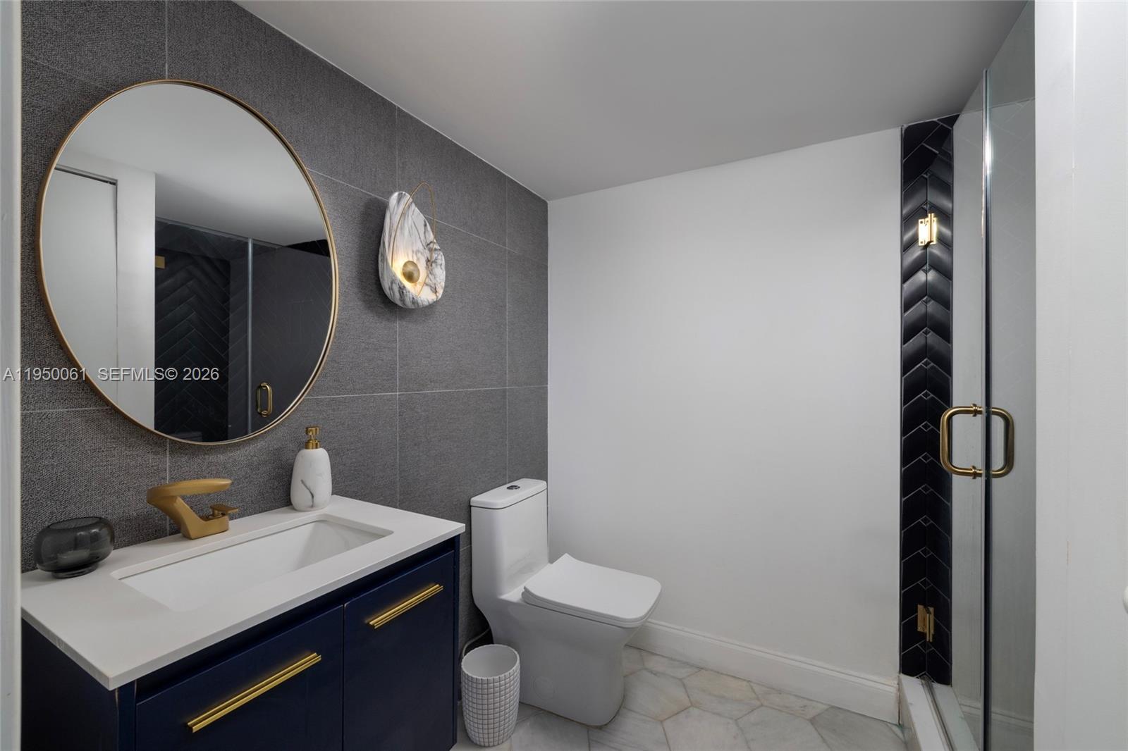 A modern bathroom features a navy vanity, gray tiled wall, round mirror, and glass shower — 4000 Towerside Ter # 804, Miami FL 33138, MIAMI, FL