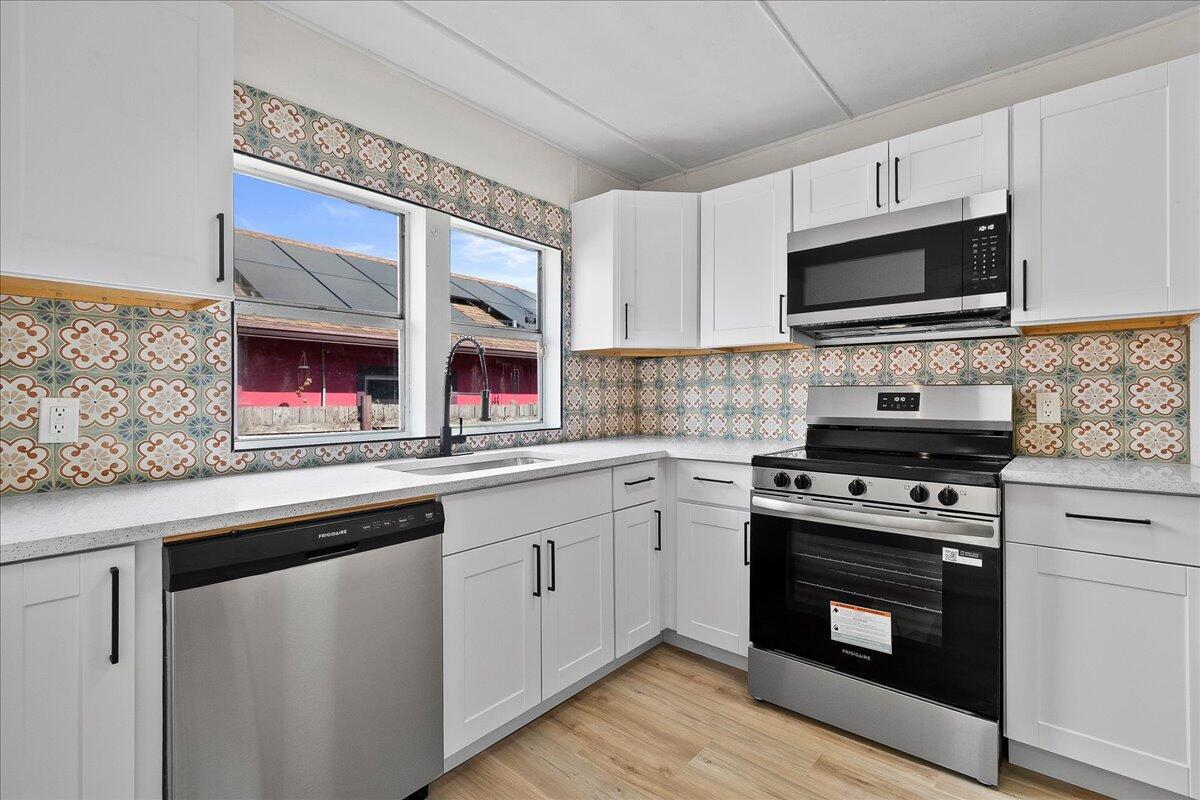 A kitchen features white cabinets, stainless steel appliances, and a patterned tile backsplash — 1011 22nd Street, West Palm Beach FL 33407, WEST PALM BEACH, FL
