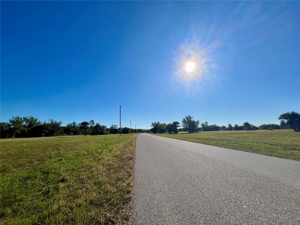 A paved road stretches through a grassy field under a bright, sunny blue sky — 17 BRIG CIRCLE E, PLACIDA, FL