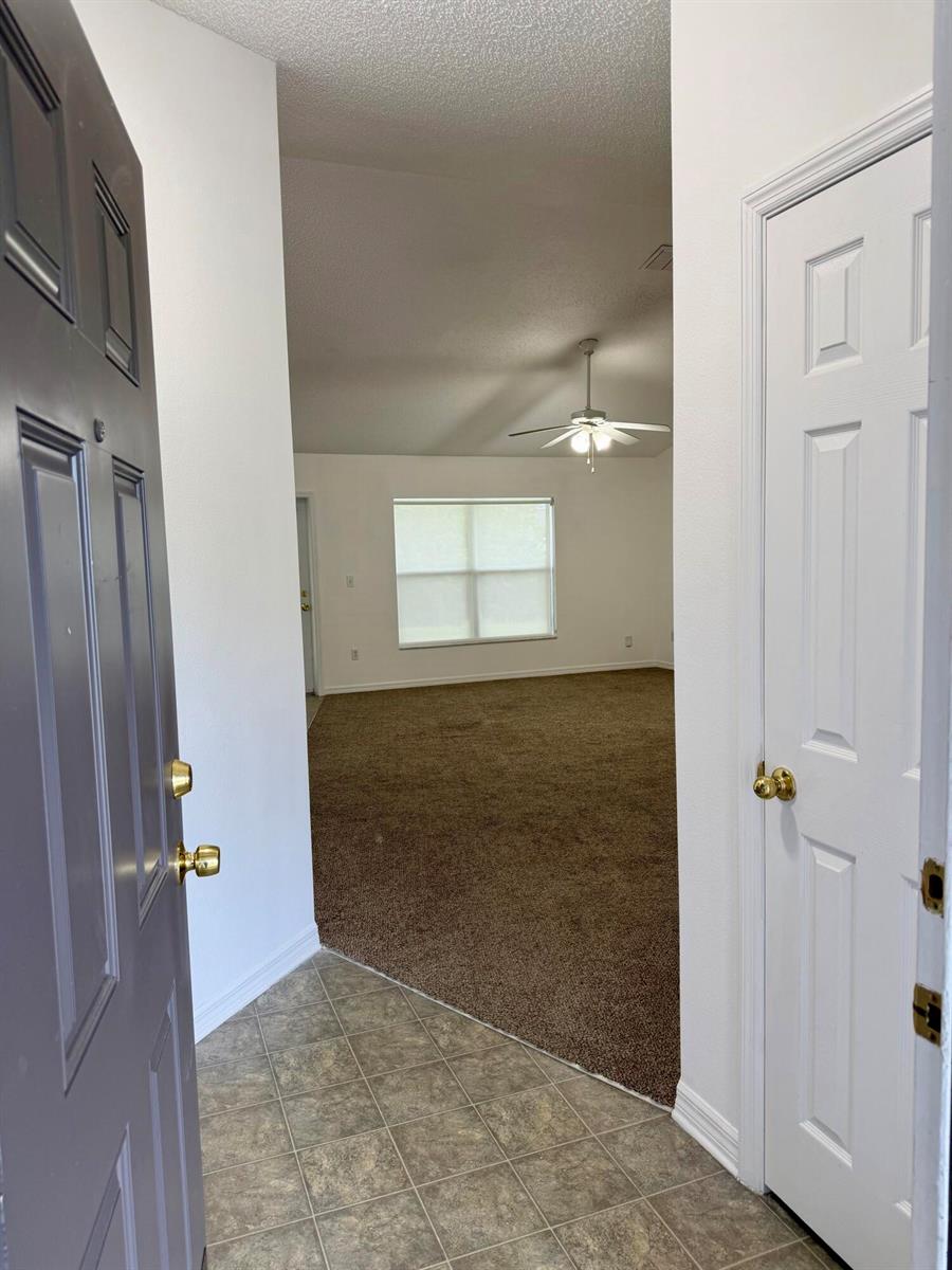 An entryway with tile flooring leads into a carpeted living room with a ceiling fan — 324 Seaside Terrace, Sebastian FL 32958, SEBASTIAN, FL