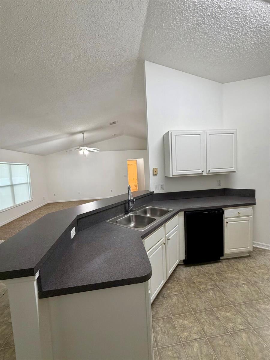 A kitchen with white cabinets, dark countertops, and a double sink overlooks a living area — 324 Seaside Terrace, Sebastian FL 32958, SEBASTIAN, FL