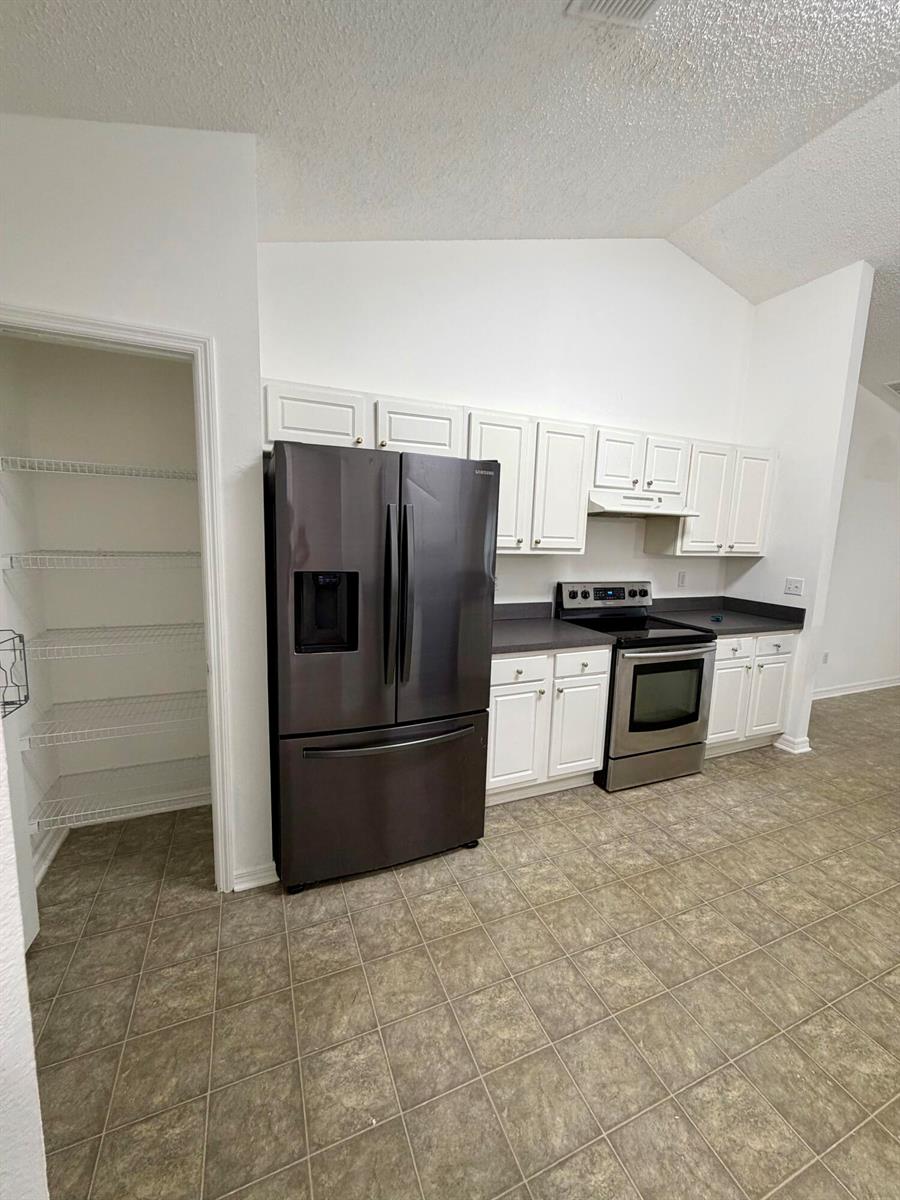 A kitchen features white cabinetry, dark countertops, stainless steel appliances, and an adjacent walk-in pantry — 324 Seaside Terrace, Sebastian FL 32958, SEBASTIAN, FL