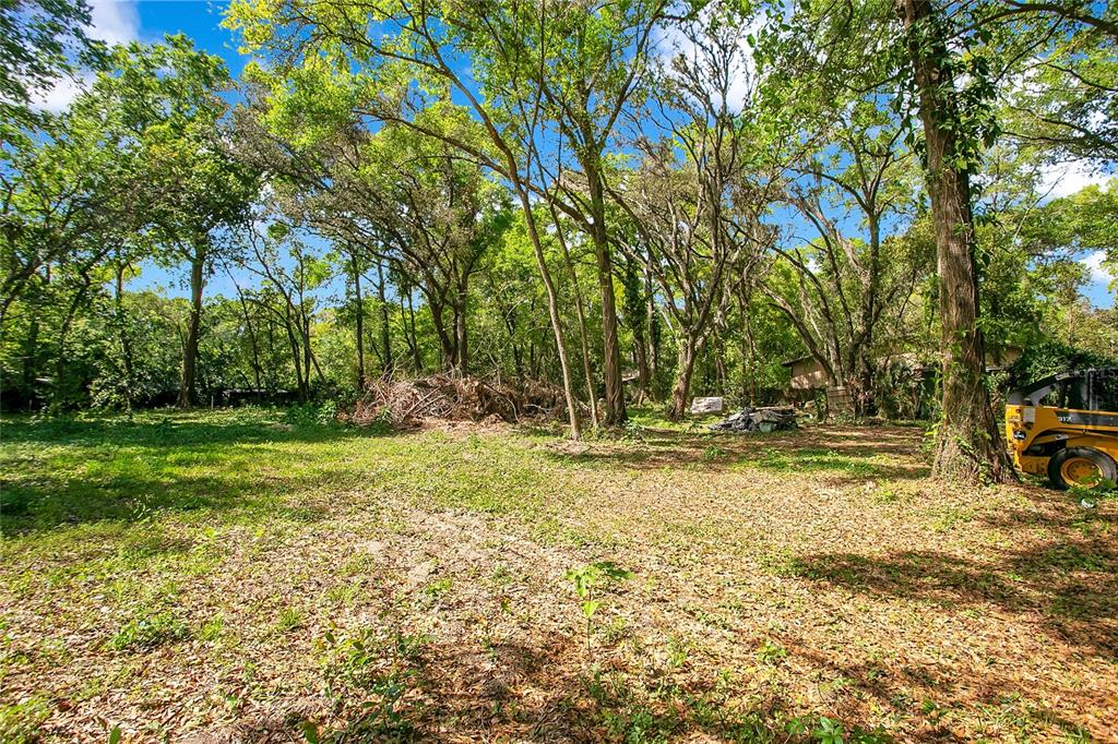 A wooded lot features a yellow skid steer parked near large trees and debris — 1120 SHEELER AVENUE, APOPKA, FL