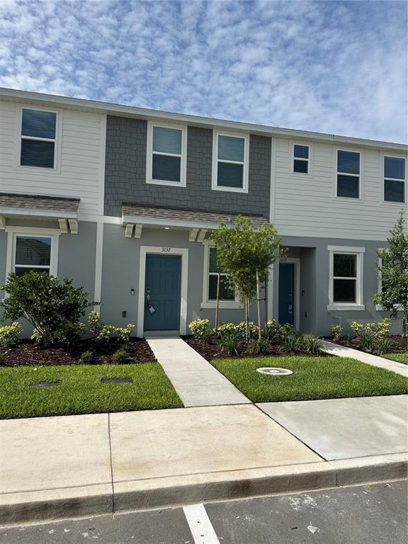 The exterior of a two-story townhouse features gray siding, a blue front door, and landscaping — 3137 SKYLINE LOOP, KISSIMMEE, FL