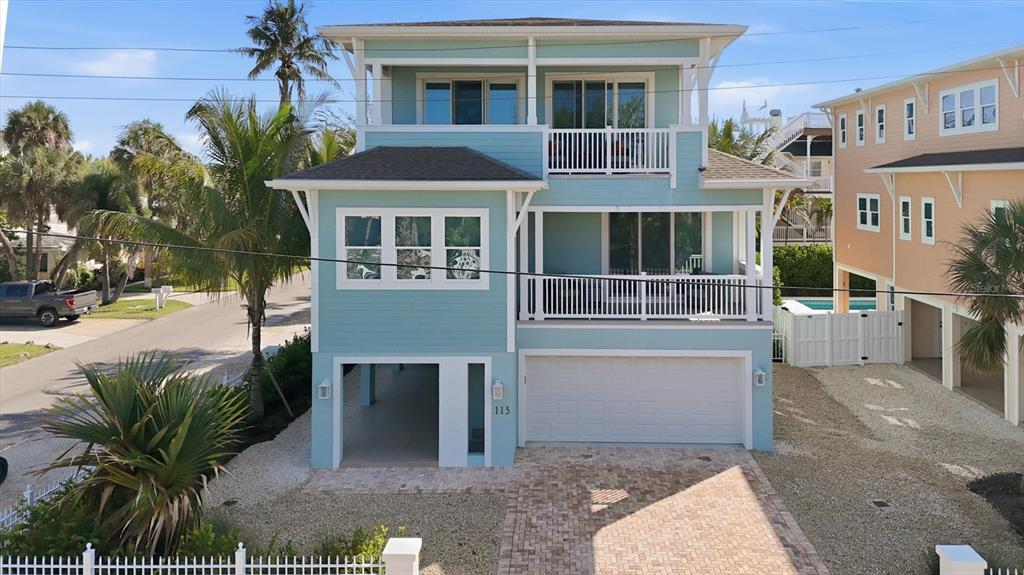 A three-story light blue coastal house features a garage, covered parking, and two balconies — 115 AQUA LANE, HOLMES BEACH, FL