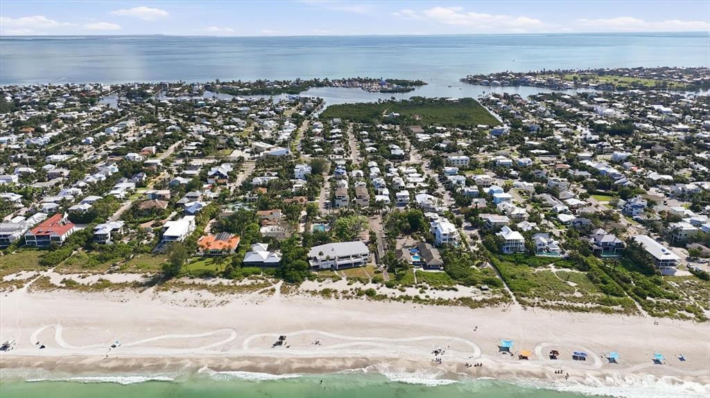 An aerial view shows a coastal neighborhood with houses situated along a sandy beach — 115 AQUA LANE, HOLMES BEACH, FL