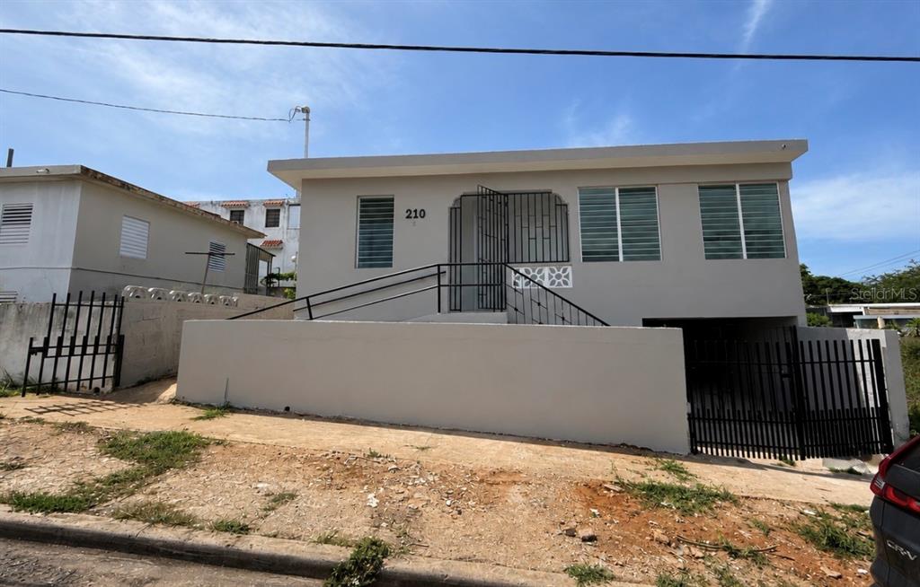 A light-colored house with a raised porch, metal railings, and a gated driveway — Zeno Gandia 65 INFANTERÍA, ARECIBO, PR