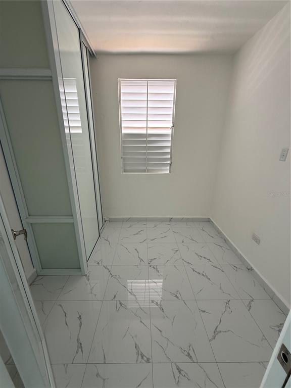 A small room with white marble-patterned tile floors and a sliding glass door closet — Zeno Gandia 65 INFANTERÍA, ARECIBO, PR