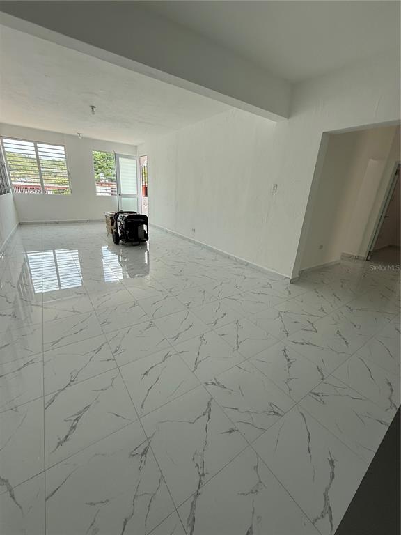 An empty room features white marble-patterned tile flooring, white walls, and large windows — Zeno Gandia 65 INFANTERÍA, ARECIBO, PR
